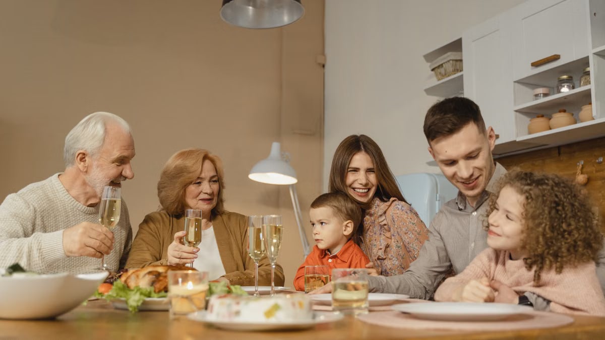 Smiling family of multiple generations enjoying a meal together indoors, sharing laughter and drinks.